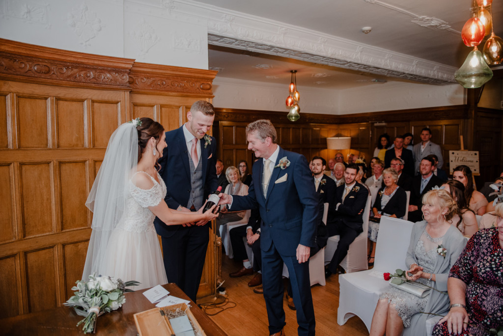Father giving the bride and groom a bottle of wine during a wine box ceremony