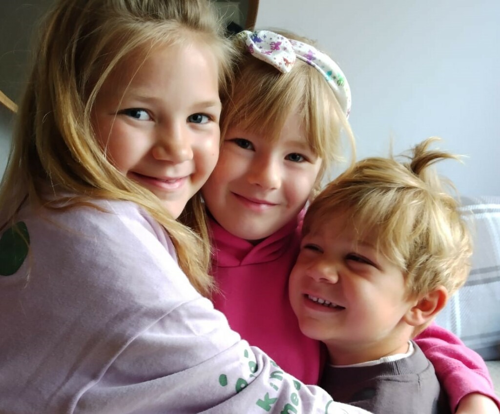 Three children smiling and hugging at naming ceremony